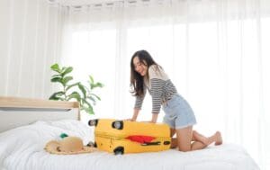 Young,Asian,Woman,Trying,To,Pack,Her,Clothes,In,To