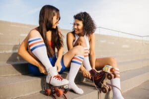 Two,Friends,Sitting,On,Steps,,Putting,On,Their,Roller,Skates