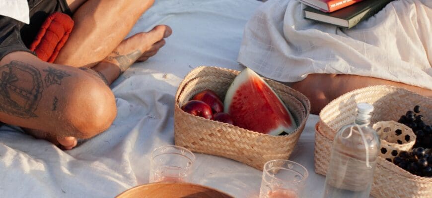 Two people enjoying an outdoor summer picnic with watermelon, apples, and books