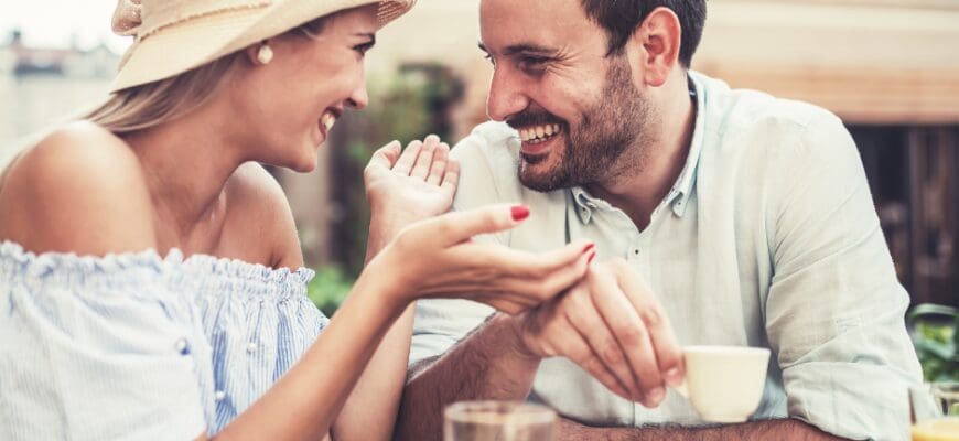 A man and woman smiling while sitting at an outdoor cafe table and drinking coffee