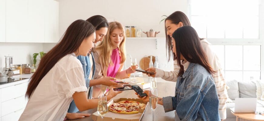 Five women gathered around a pizza on a kitchen island in a bright apartment