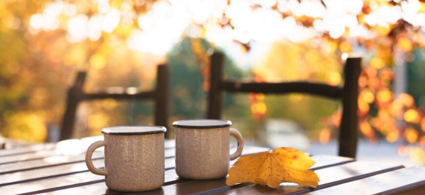 Two mugs on top of a wooden table outdoors